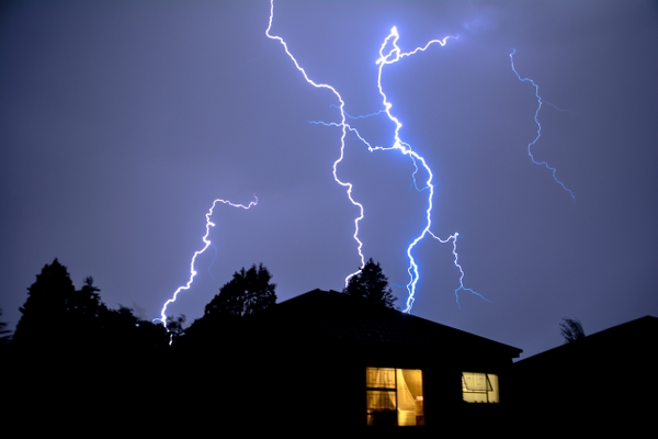 Lightning striking during a storm near a house with illuminated windows, emphasizing the importance of generator installation for safety during unpredictable weather in Ocean Pines, Maryland.